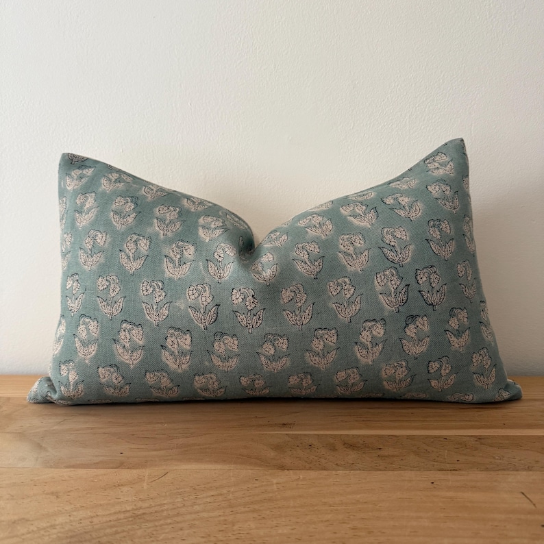 May include: A teal blue pillow with a white floral pattern. The pillow is made of a soft, comfortable fabric and has a subtle sheen.