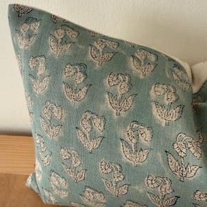 May include: A blue pillow cover with a white floral pattern. The fabric has a subtle texture and the flowers are outlined in black.