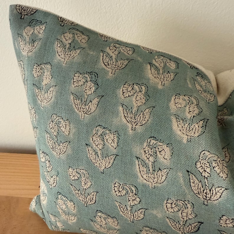 May include: A blue pillow cover with a white floral pattern. The fabric has a subtle texture and the flowers are outlined in black.