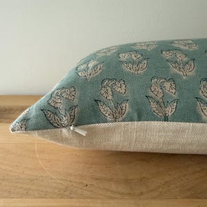 May include: A light blue throw pillow with a white floral pattern. The pillow has a zipper closure and a light beige backing.