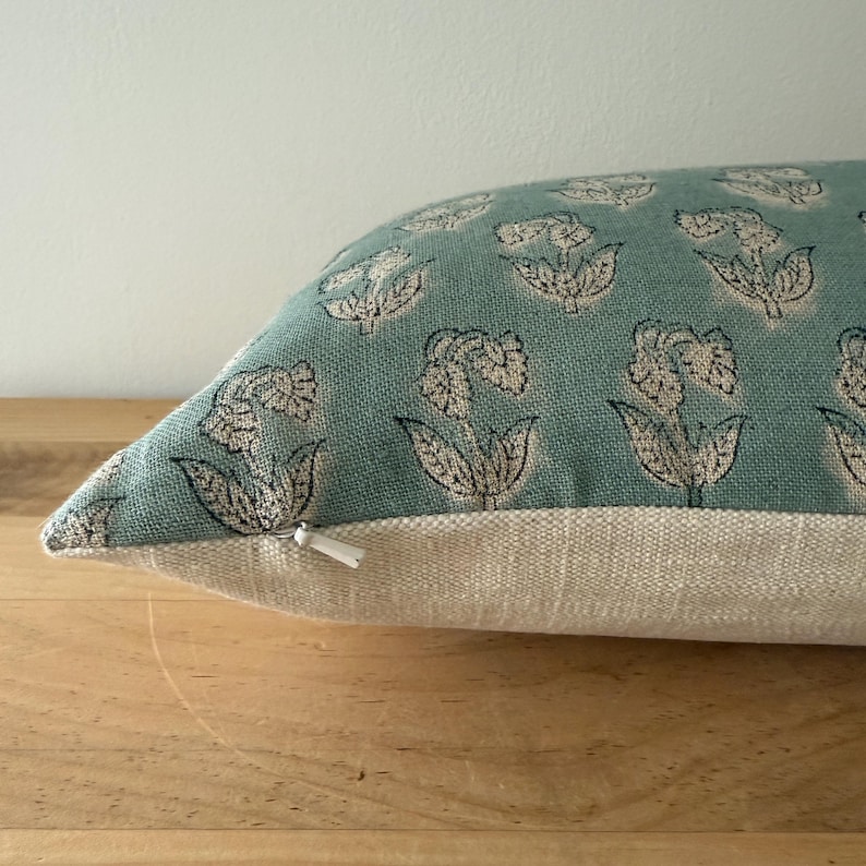 May include: A light blue throw pillow with a white floral pattern. The pillow has a zipper closure and a light beige backing.