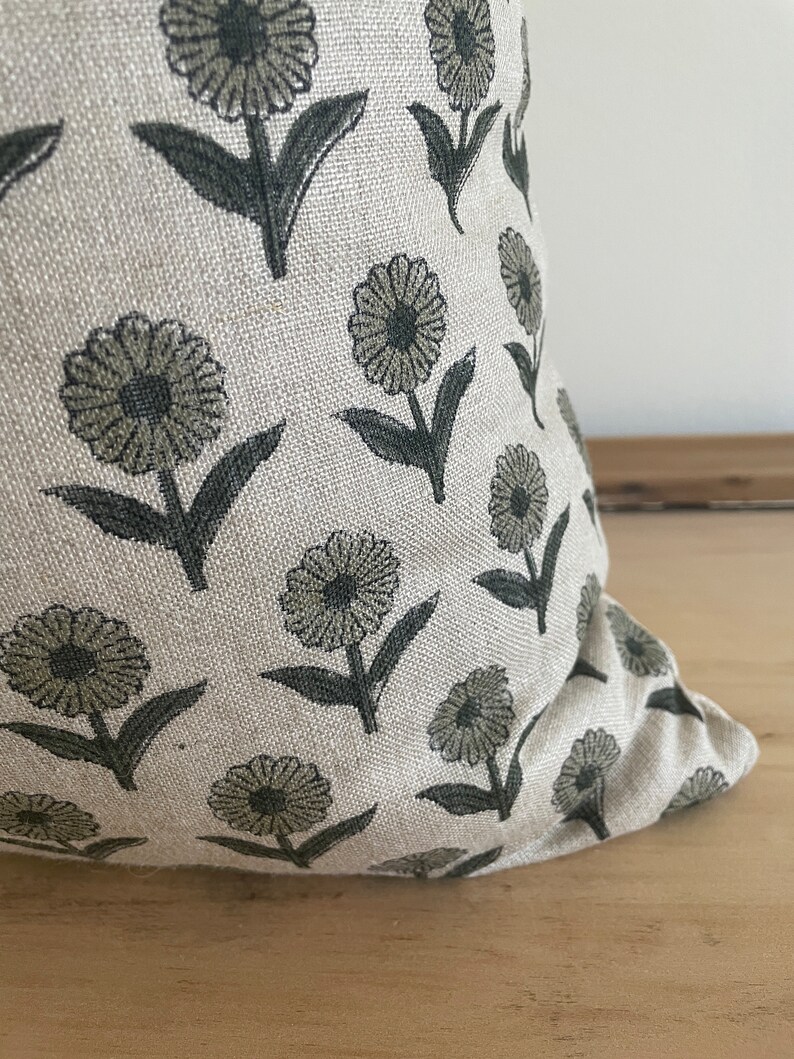 May include: A decorative pillow with a floral pattern. The pillow features a repeating design of stylized flowers in shades of gray and green on a light beige background. The pillow is made of a textured fabric.