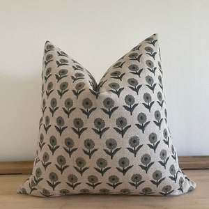 May include: A decorative throw pillow with a floral pattern. The pillow features a repeating design of dark gray flowers on a light beige background. The pillow is made of a soft fabric and is designed for home decor.