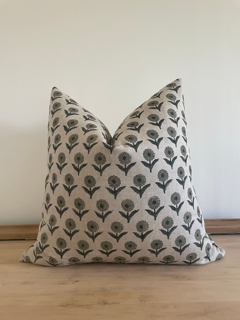May include: A decorative throw pillow with a floral pattern. The pillow features a repeating design of dark gray flowers on a light beige background. The pillow is made of a soft fabric and is designed for home decor.