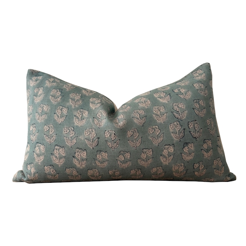May include: A teal blue pillow with a floral pattern in pink and black. The pillow is made of a soft, textured fabric.