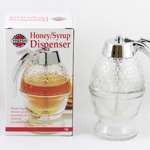 May include: A clear glass honey or syrup dispenser with a chrome handle and a honeycomb pattern. The dispenser has a trigger mechanism to release the honey or syrup. The box reads "Honey/Syrup Dispenser" and "NORPRO".