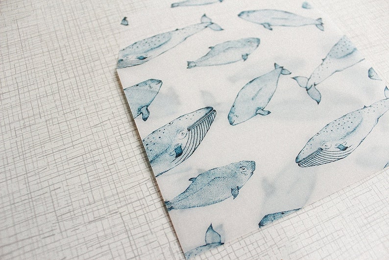 May include: White paper with a pattern of blue whales. The whales are illustrated in a watercolor style, with details like fins, tails, and textured bodies. The paper is partially visible, with a textured, light gray surface in the background.