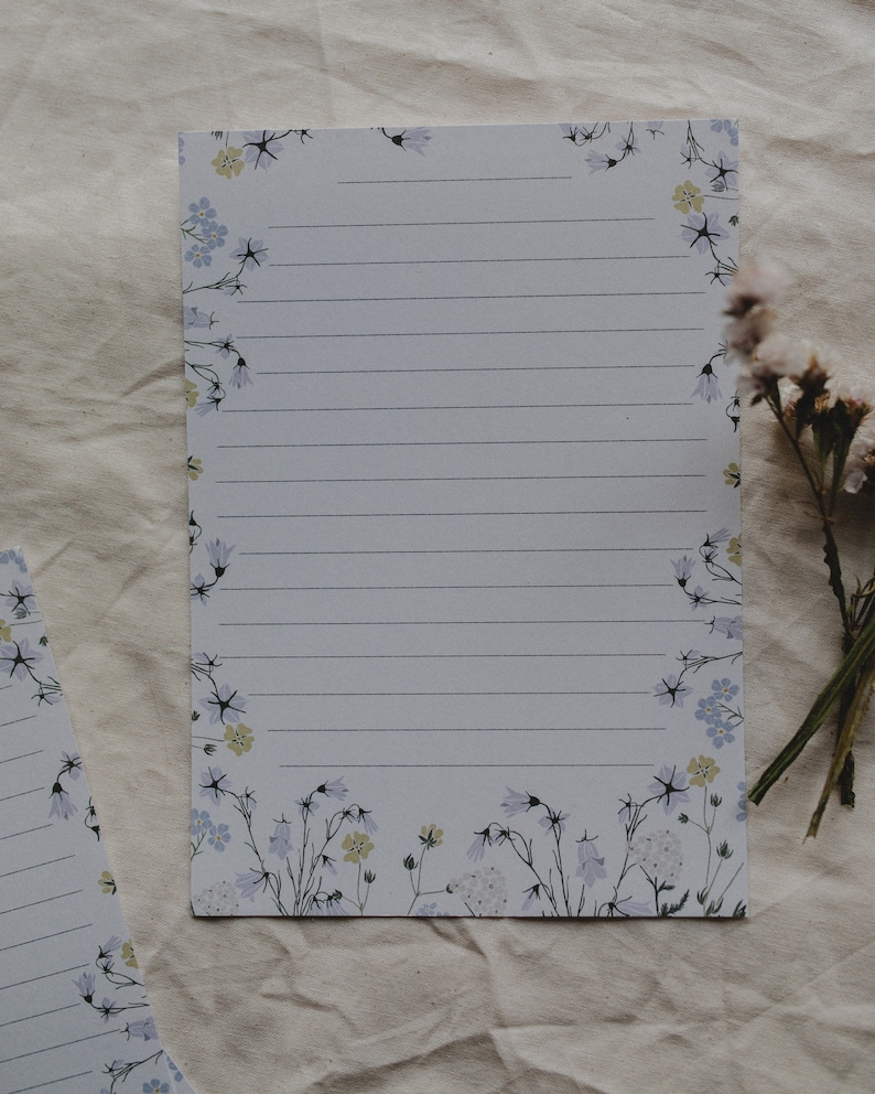 May include: A white sheet of lined paper with a floral border. The border features small blue and yellow flowers with green stems.