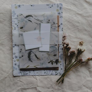 May include: A set of letter writing stationery featuring a floral design and a translucent sheet with pressed flowers. The set includes envelopes and letter paper. The label reads "letter writing set".
