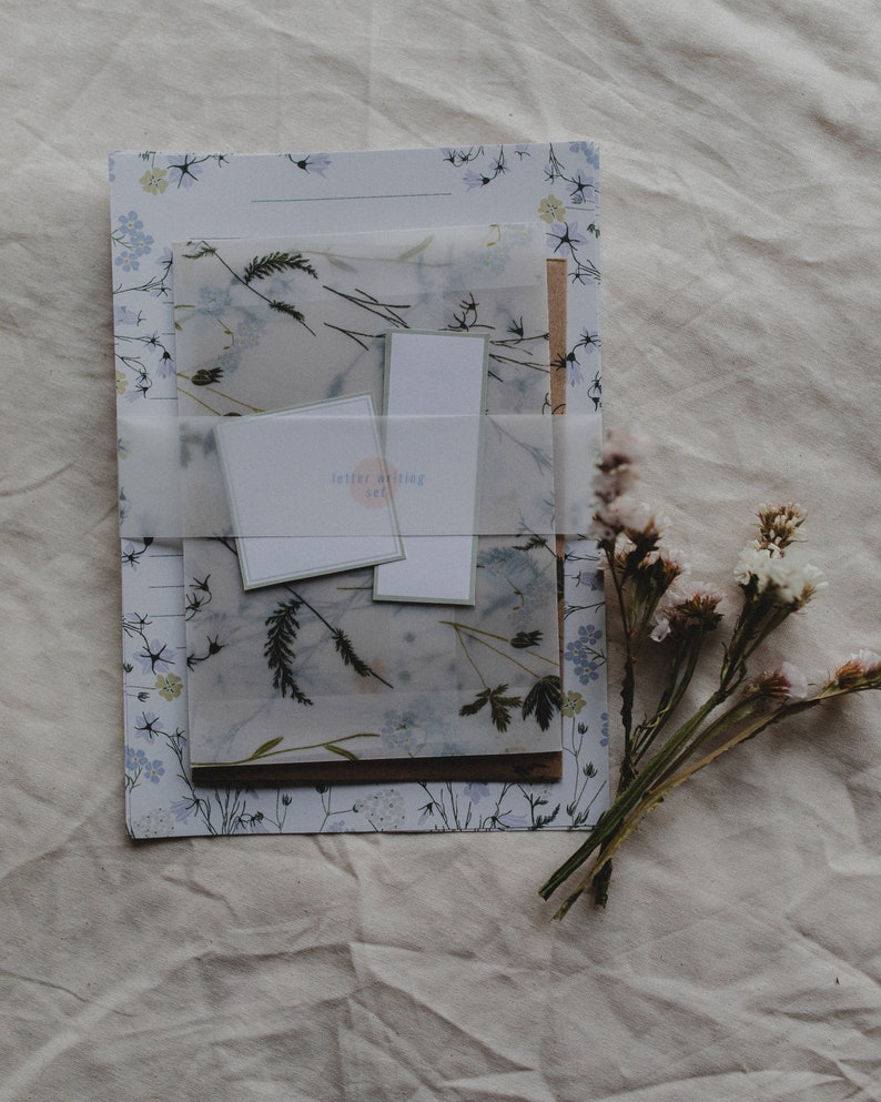 May include: A set of letter writing stationery featuring a floral design and a translucent sheet with pressed flowers. The set includes envelopes and letter paper. The label reads "letter writing set".
