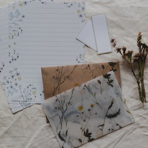 May include: A set of stationery featuring a floral design with blue and white flowers. The stationery includes a sheet of lined paper, a blank card, and a brown envelope with a floral design.
