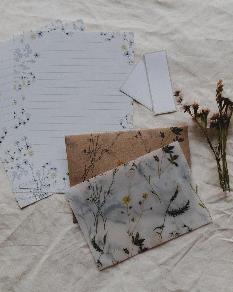May include: A set of stationery featuring a floral design with blue and white flowers. The stationery includes a sheet of lined paper, a blank card, and a brown envelope with a floral design.