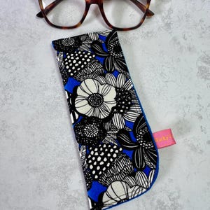 May include: A glasses case with a blue and white floral design and a pink tag. The case features a black and white floral pattern with a blue interior. Tortoiseshell glasses are positioned above.