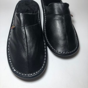 May include: A pair of black leather slippers with white stitching around the soles. The interior of the slippers is lined with black fur. The slippers are designed for indoor use and provide comfort and warmth.