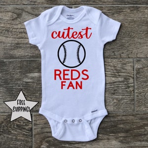 Peut inclure: Combinaison blanche pour bébé avec le texte rouge "cutest reds fan" et un graphique de baseball noir.