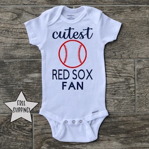 Peut inclure: Combinaison blanche pour bébé avec un ballon de baseball rouge et un texte bleu qui dit "cutest red sox fan".