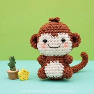Peut inclure: Un singe en crochet avec une fourrure brune, un visage blanc et des yeux noirs. Le singe est assis avec sa queue enroulée derrière lui.