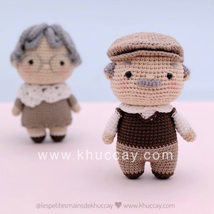 Puede incluir: Dos muñecas amigurumi de crochet, una con cabello gris y gafas, la otra con un sombrero marrón y bigote. Ambas muñecas visten ropa marrón y beige.