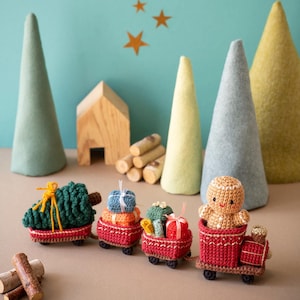 May include: A red toy train with a gingerbread person conductor, carrying a Christmas tree and presents. The train is surrounded by felt trees and a wooden house.