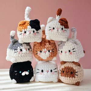 May include: A stack of eight crocheted cat plushies in various colours, including black, white, grey, brown, and orange. The plushies are all in a sitting position with their paws tucked under them. The plushies are all made with a soft, fluffy yarn.