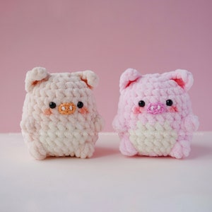 May include: Two crocheted pig plushies, one in pink and one in white, with black eyes and pink noses.