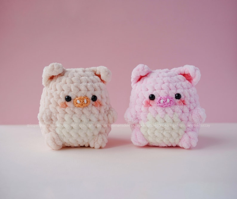 May include: Two crocheted pig plushies, one in pink and one in white, with black eyes and pink noses.