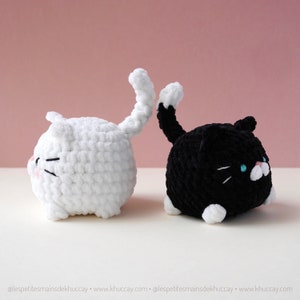 May include: Two crocheted cat plushies, one white and one black, with white yarn accents. The white cat is facing left and the black cat is facing right.