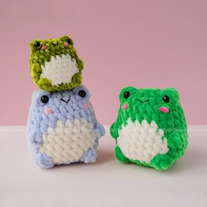 May include: Three crocheted frog plushies. The largest frog is green, the middle frog is blue, and the smallest frog is green. All three frogs have white bellies.