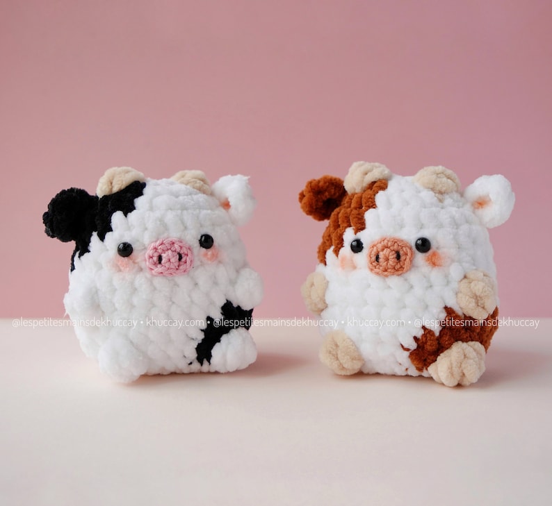 May include: Two crocheted stuffed cows, one black and white and one brown and white. Both cows have pink noses and black eyes.