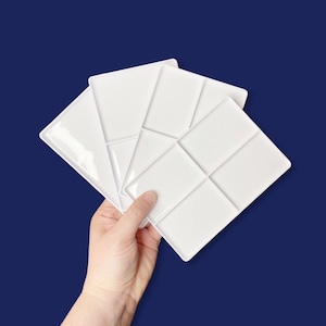 May include: Three white plastic paint palettes with six wells each. The palettes are stacked on top of each other.