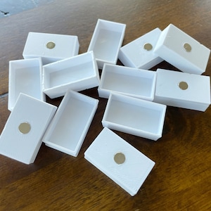 以下が含まれることがあります： 各箱の上部に小さな丸い磁石が付いた、白い長方形の箱が10個あります。