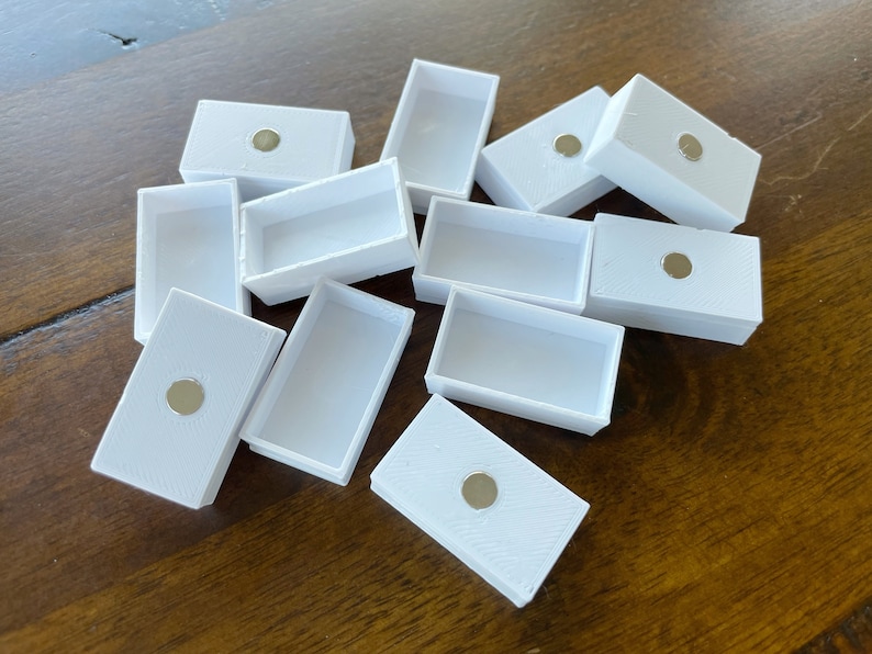 以下が含まれることがあります： 各箱の上部に小さな丸い磁石が付いた、白い長方形の箱が10個あります。