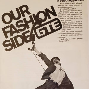 May include: A woman in a suit jumps in the air holding a phone with a cord. The phone is connected to a large sign that says "Our Fashion Side GTE". The sign is black and white. The woman is holding a bag that says "GTE Phone Mart" in black and white.