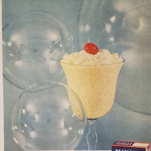 May include: A glass of Minute Tapioca Cream dessert topped with a red cherry. The dessert is light and fluffy, and the box of Minute Tapioca is in the lower right corner of the image. The box is blue and white with the words "Minute Tapioca" in bold, red letters. The box also says "Quick-Cooking!" and "Makes 36 servings".