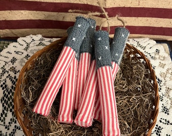 May include: Five red and white striped fabric firecrackers with blue denim tops. The firecrackers are in a brown wicker basket filled with brown shredded paper.
