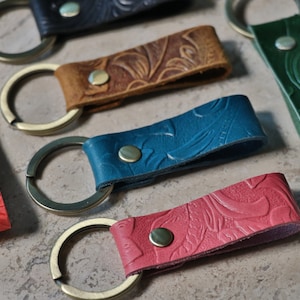 Puede incluir: Surtido de seis llaveros de cuero con diferentes patrones en relieve de colores. Cada llavero tiene un anillo de llave de latón.