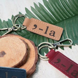 May include: Two leather keychains with metal rings and clasps. The keychains are brown and red and have the text "9-la" embossed on them.