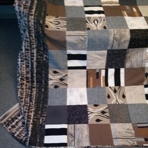 May include: A patchwork quilt featuring a mix of brown, grey and white fabrics. The quilt is composed of squares and rectangles in various sizes and patterns.