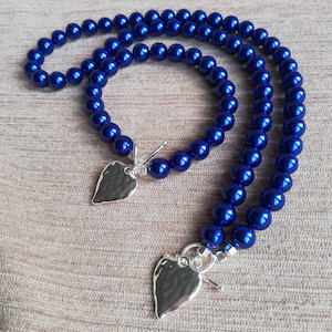 May include: A set of two necklaces featuring blue pearl beads and silver heart pendants. The necklaces are layered and have a clasp fastening.