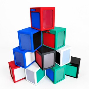 May include: A pyramid stack of ten multi-colored plastic cubes. Each cube features a solid frame in red, blue, green, white, or black, with a contrasting colored panel on the front and side faces. Small rectangular buttons are visible on the top edges.