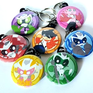 May include: A selection of round keyrings with cartoon character designs in various colours. Each keyring displays a different character, with shades of red, green, blue, and yellow. The keyrings are attached to silver keychains.