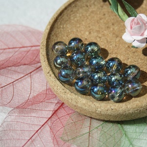 Peut inclure: Gros plan sur un petit bol rempli de perles de verre bleues irisées. Le bol est en liège et a une couleur brun naturel. Les perles sont disposées de manière aléatoire et réfléchissent la lumière.