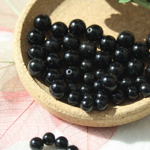 以下が含まれることがあります： 光沢のある黒いビーズのコレクション。各ビーズは滑らかな球形をしています。ビーズは、小さくて丸いコルクの皿に展示されています。背景には、赤と白の繊細な葉のような模様があります。