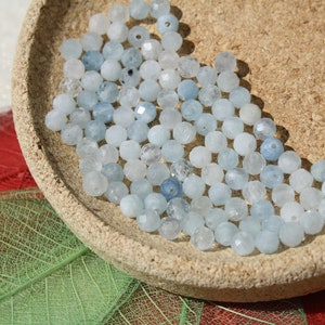 May include: A bowl of light blue aquamarine beads. The beads are round and have a slightly faceted finish.