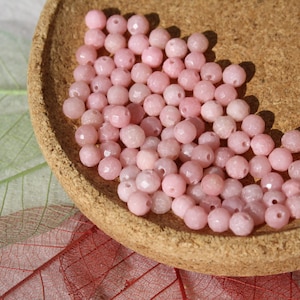May include: A bowl of pink opal beads. The beads are round and have a faceted finish. They are perfect for jewelry making.