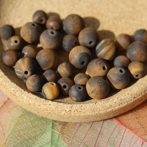 Peut inclure: Un bol de perles en œil de tigre brun et or. Les perles sont rondes et ont une finition lisse et polie.