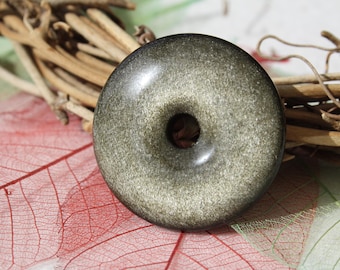 Könnte beinhalten: Ein runder, grauer Goldstone-Anhänger mit einem Loch in der Mitte. Der Anhänger hat eine gesprenkelte, glitzernde Optik.