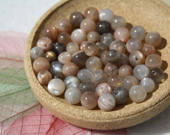 May include: A bowl of iridescent sunstone beads in shades of gray, brown, and white. The beads are round and have a smooth, polished finish.