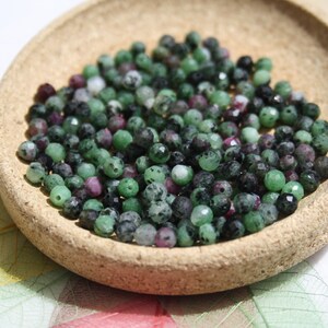 Peut inclure: Un bol de perles de pierres précieuses vertes, noires et roses. Les perles sont facettées et ont un aspect moucheté.