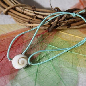 Peut inclure: Un bracelet élastique turquoise avec un charme en coquillage blanc. Le coquillage a un motif en spirale.